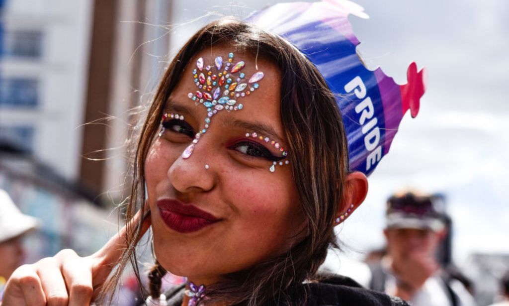 This is an image of a Columbian queer person at a Pride parade in Bogata, Columbia. They have jewels across their forehead and have on red lipstick.