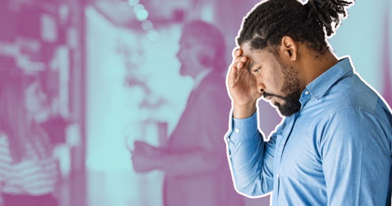 This is an image of a Black man looking frustrated while leaning on a wall. He has short dread locks tied up behind his head. He has a beard and is wearing a blue shirt.