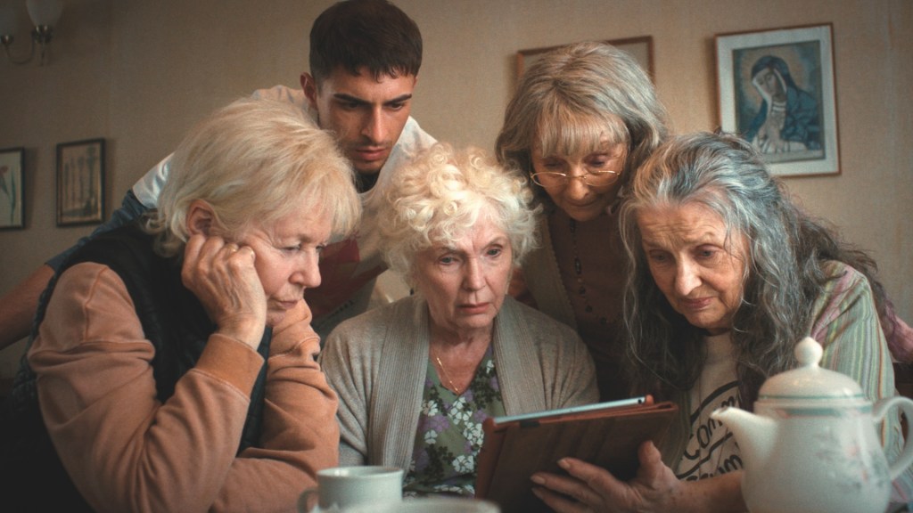 Four Mothers still of four older women looking at an iPad as a younger man joins them