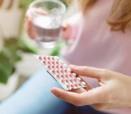 Femme-presenting person holding a pack of contraceptive pills and a glass of water.