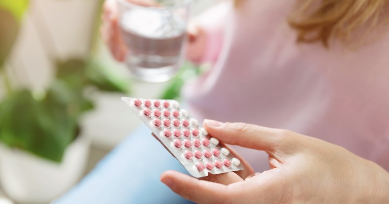 Femme-presenting person holding a pack of contraceptive pills and a glass of water.