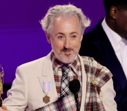 Alan Cumming on stage at the Emmys, holding his award, close cropped to show the trans pride flag medal