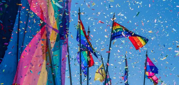 This is an image of confettie flying amongst large Pride flags on a sunny day.