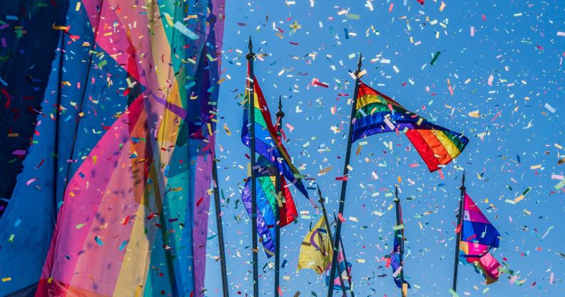 This is an image of confettie flying amongst large Pride flags on a sunny day.