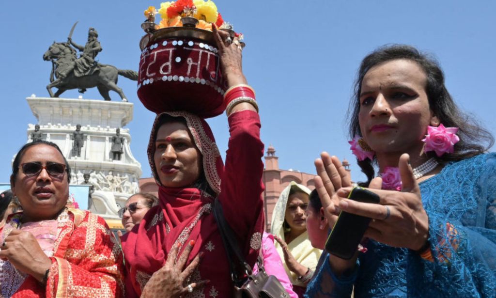 This is an image of 3 Asian transgender women. One is clapping and the other is holding a bucket of flowers on her head. 