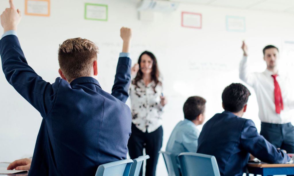 A group of school students raising their hands.