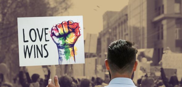 This is an image of someone holding a protest sign that reads "Love Wins" in a protest. The sign is being held by a man with short hair facing away from the camera. The sign is in full colour while the rest of the image is in a sepia tone