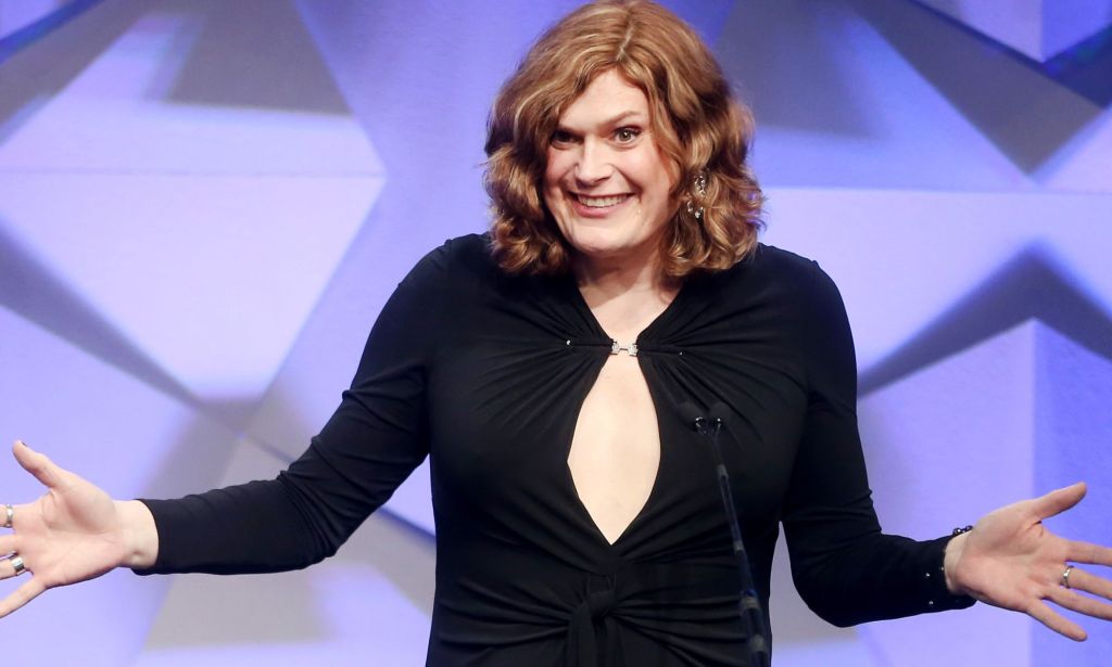 Lilly Wachowski, in a black dress, speaking at an event into a microphone.