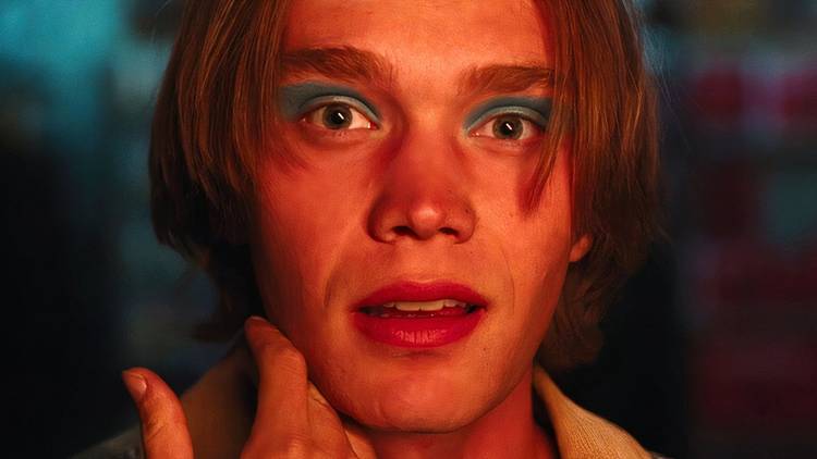 National Anthem still: Charlie Plummer in drag, bright blue eyeshadow, staring at himself