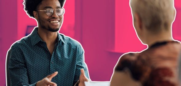 This is an image of a job interview. There is a Black man with glasses speaking to a white women with blond hair.