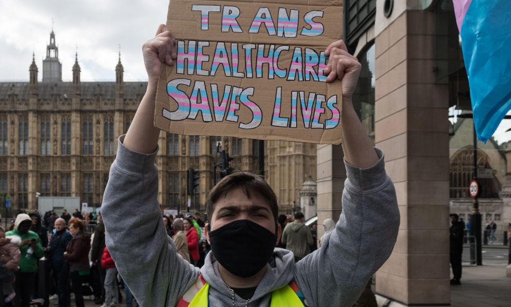 A person holding a sign that reads "trans healthcare saves lives."