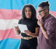 This is an image of two trans employees looking down at a tablet over the trans pride flag.