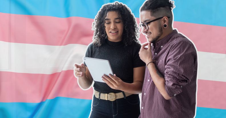 This is an image of two trans employees looking down at a tablet over the trans pride flag.