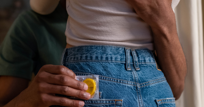 Couple embracing, with one person holding a condom.