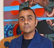 Waheed Alli attends the launch of new exhibition "Filling In The Pieces In Black". He's standing in front a piece of colourful arwork in a blue suit