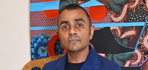 Waheed Alli attends the launch of new exhibition "Filling In The Pieces In Black". He's standing in front a piece of colourful arwork in a blue suit