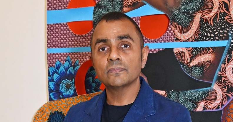 Waheed Alli attends the launch of new exhibition "Filling In The Pieces In Black". He's standing in front a piece of colourful arwork in a blue suit