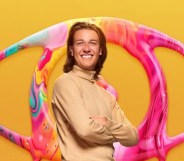 Big Brother Nathan wearing a rollneck in front of a yellow background and eye logo