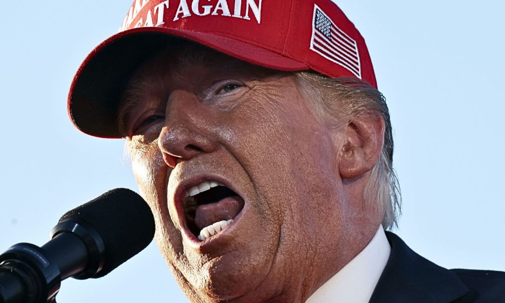 Donald Trump speaking with his mouth open into a microphone.