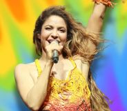 Shakira performing against a rainbow background.