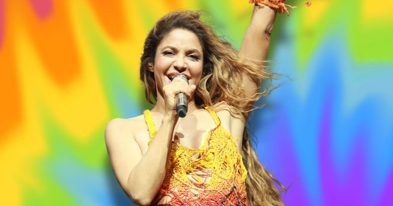 Shakira performing against a rainbow background.