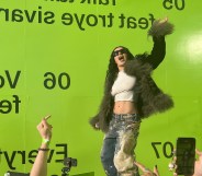 Charli XCX shared her new remix album with a few hundred fans at a special event. Huge lime green wall behind charli in distressed jeans, cropped white top and fuzzy jacket.