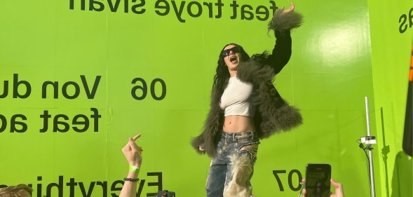 Charli XCX shared her new remix album with a few hundred fans at a special event. Huge lime green wall behind charli in distressed jeans, cropped white top and fuzzy jacket.