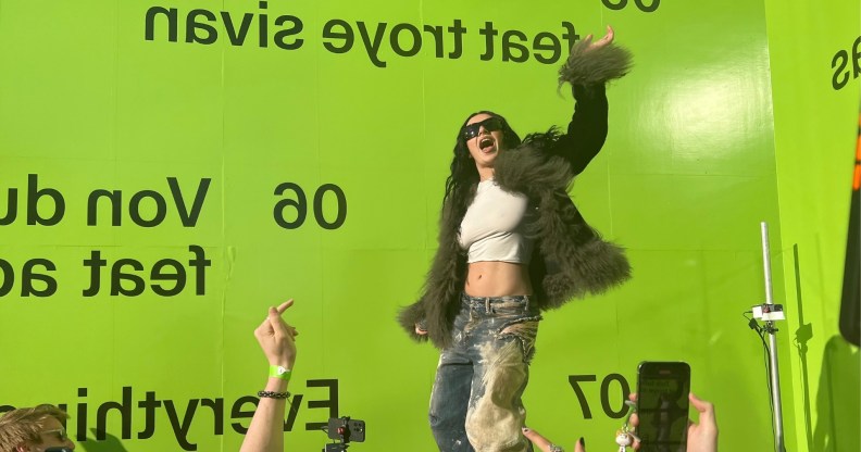 Charli XCX shared her new remix album with a few hundred fans at a special event. Huge lime green wall behind charli in distressed jeans, cropped white top and fuzzy jacket.