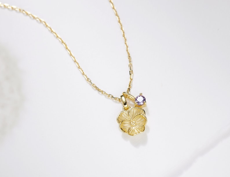 A gold violet necklace with a violet shaped charm and a violet coloured charm on the chain