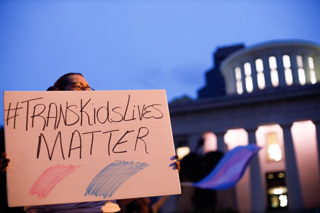 Trans rights activist holding sign which reads, "Trans kids lives matter".