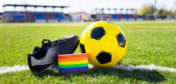 Rainbow colors of LGBTQ+ Pride on an armband next to a football and football boot.