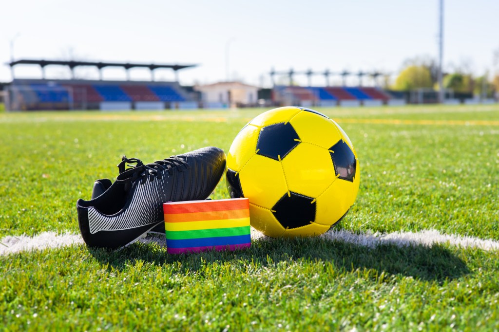 Rainbow colors of LGBTQ+ Pride on an armband next to a football and football boot.