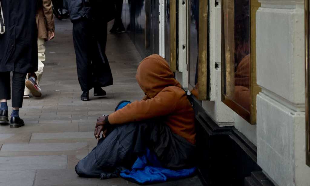 A homeless person sits in front of a theatre as people walk past in London.