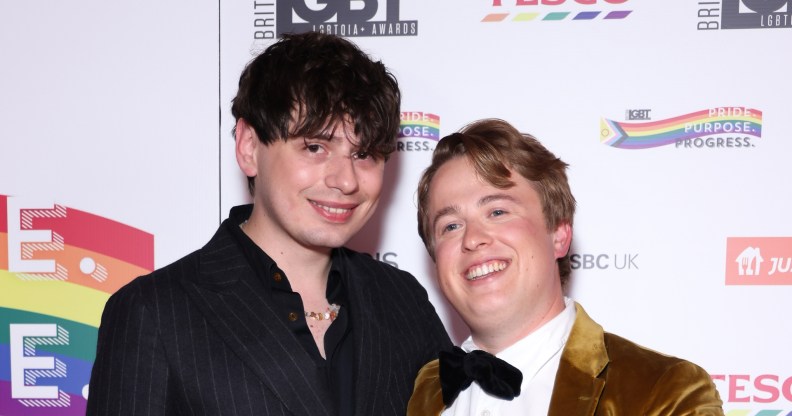 Jordan Sangha and Henry Southan poses with the Media Moment award. Jordan in a dark pinstripe suit and Henry in a gold suit with a black bowtie.