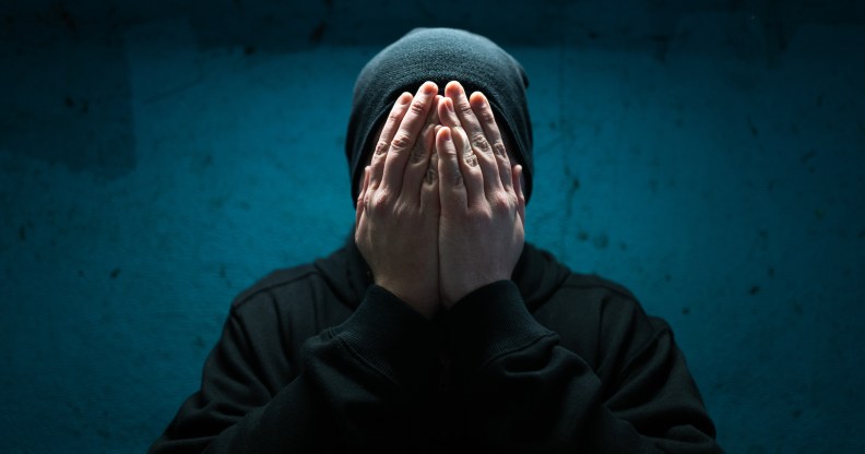 Color image depicting an adult man wearing a black beanie hat in an underground subway tunnel. His expression is one of despair, sadness and depression. His hands are covering his face in a gesture of bleak desperation and hopelessness.