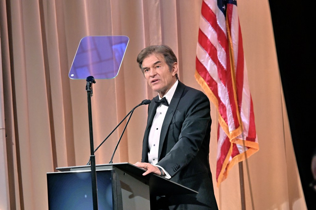 Mehmet Oz attends Ellis Island Medals Of Honor Ceremon, he's standing at a speaking podium with a US flag handing behind him