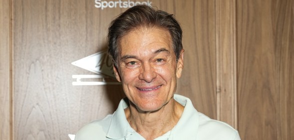 Mehmet Oz wearing a white polo top agains a wooden background