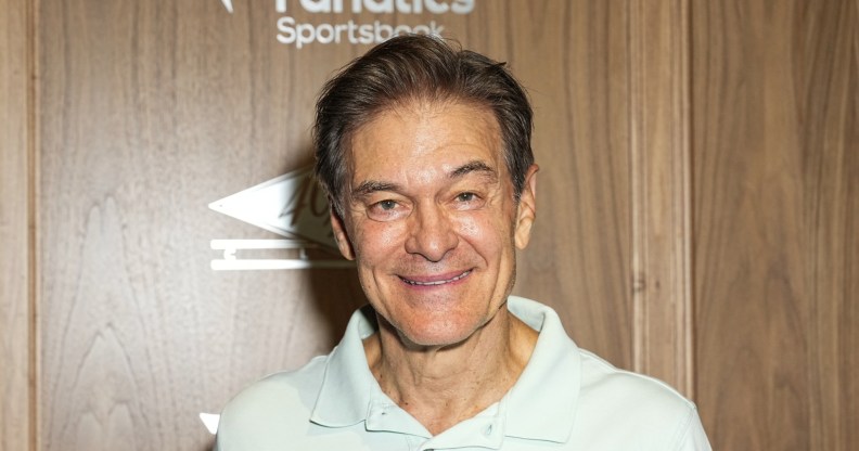 Mehmet Oz wearing a white polo top agains a wooden background