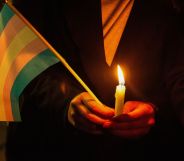 A person holding a candle and a trans flag.