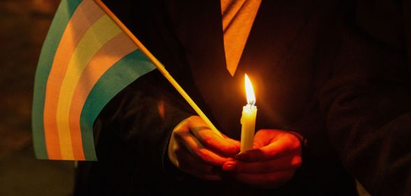 A person holding a candle and a trans flag.