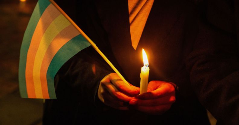 A person holding a candle and a trans flag.