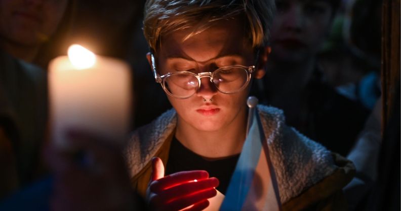 A person holds a candle and a trans flag at the vigil for murdered schoolgirl Brianna Ghey