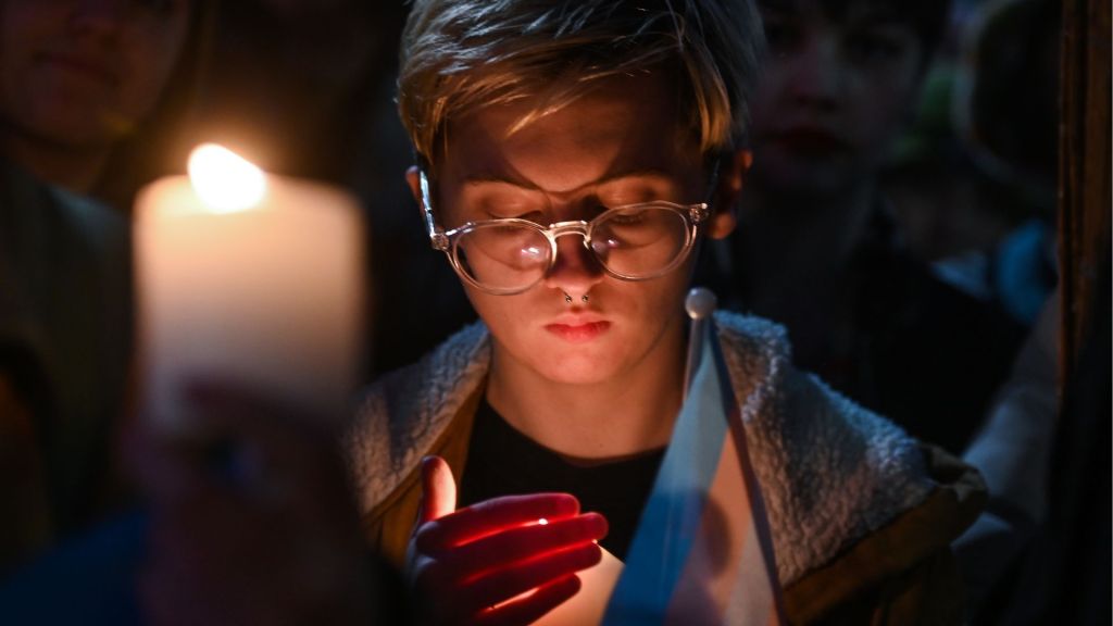 A person holds a candle and a trans flag at the vigil for murdered schoolgirl Brianna Ghey