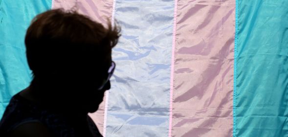 The silhouette of a person infront of a trans flag.