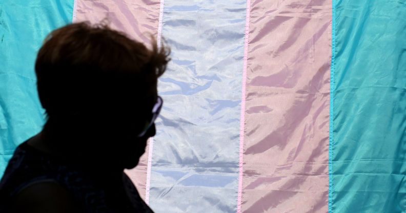 The silhouette of a person infront of a trans flag.