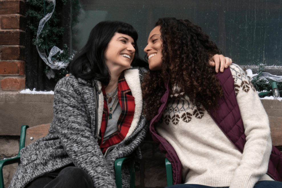 Under the Christmas Tree still; two women in Christmas jumpers leaning close