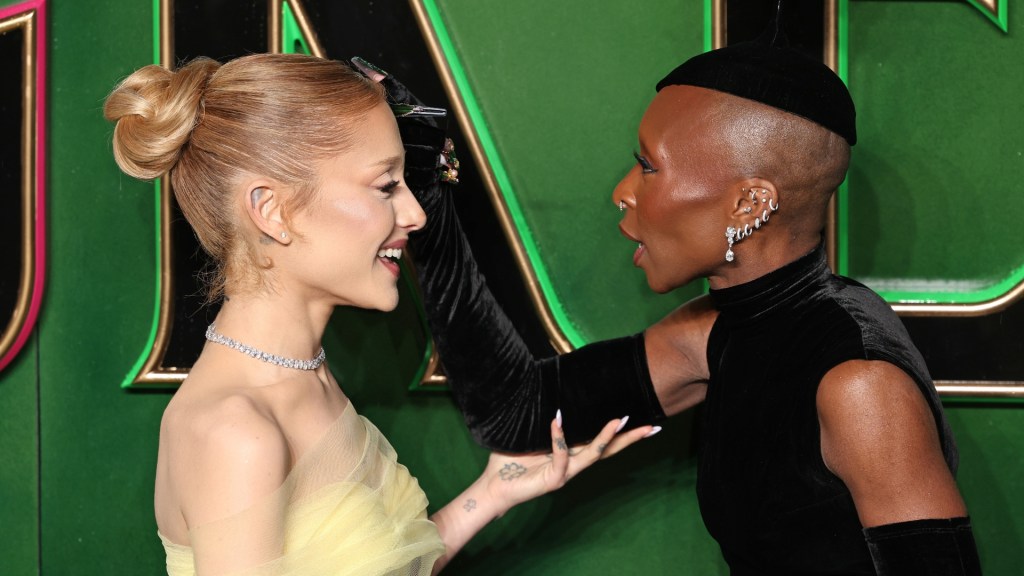 Ariana Grande and Cynthia Erivo at the "Wicked: Part One" European Premiere at The Royal Festival Hall. Grande in a yellow mesh dress and Erivo in a dark velvet dress with matching gloves and hat.