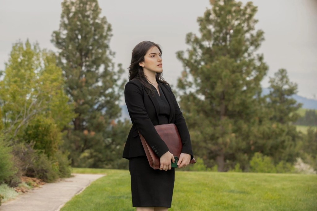 Yellowstone still of Lilli Kay in a black suit holding a brown briefcase in front of her