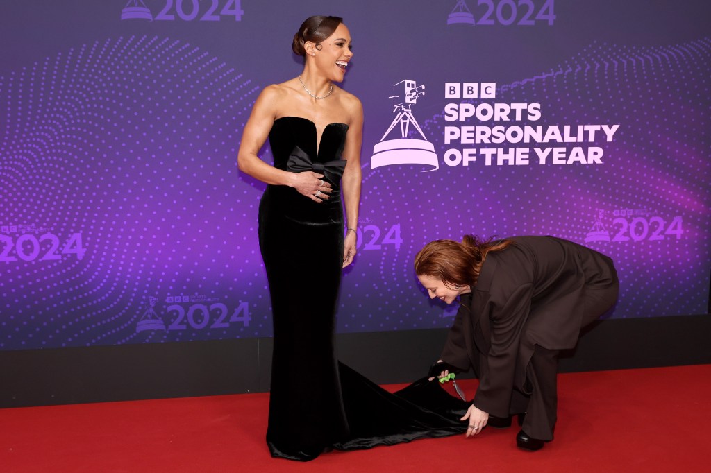 Alex Scott stands in a black gown while her girlfriend Jess Glynne adjusts it at the bottom. 