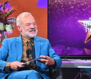 The Graham Norton Show, Graham Norton, in a blue suit, sitting next to a screen with the show name.